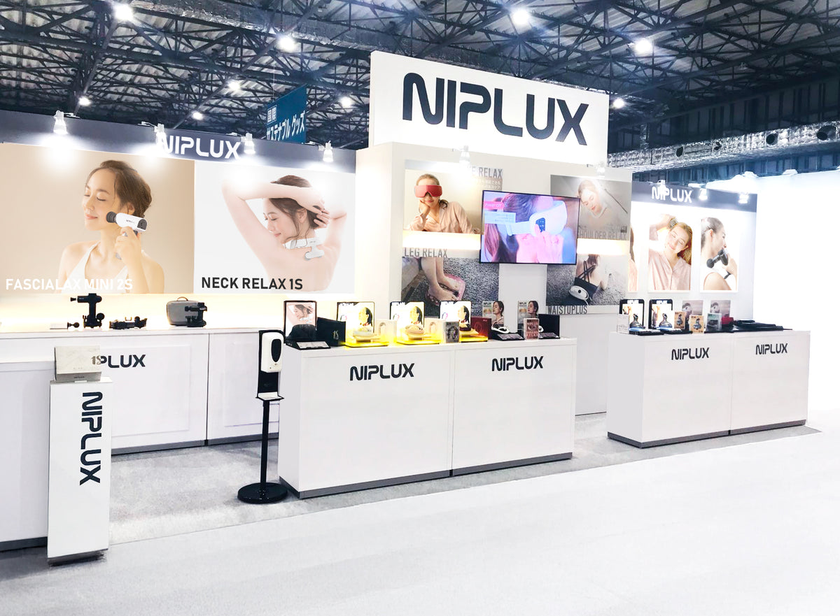 白色 NIPLUX 展台全景，設有品牌展示牆及多個產品體驗台